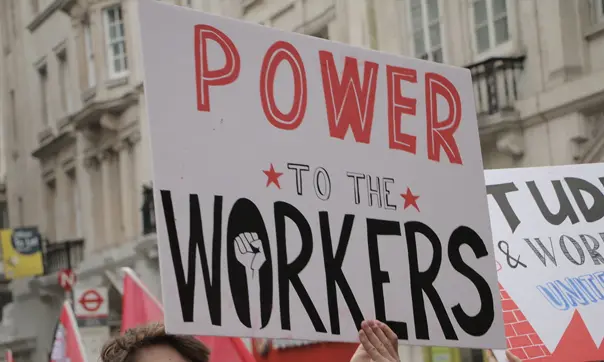 a hand-drawn protest sign reads POWER TO THE WORKERS but we can't see people's faces, etc