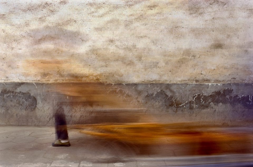 A foot plants on the ground as a person is a seen as just an orange blur of movement against a wall, only their foot is still/focused